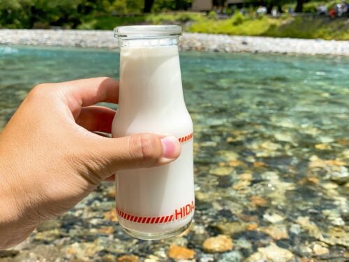 上高地の透き通った清流沿いに座って飲む便の牛乳