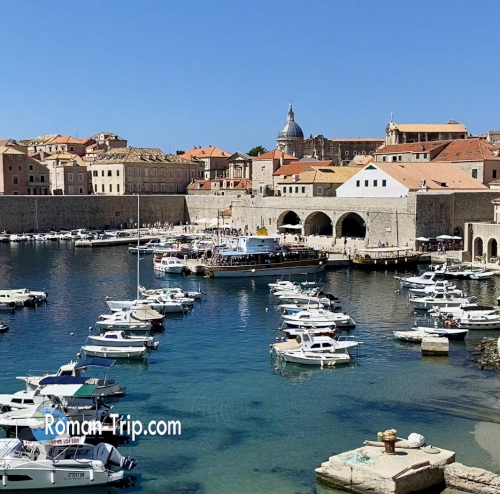 ドゥブロブニク旧港の美しい風景。青く澄んだ海にボートが並び、赤い屋根の旧市街が背景に広がる。/ A stunning view of Dubrovnik’s Old Port, with boats floating on the clear blue sea and the red-roofed Old Town in the background.