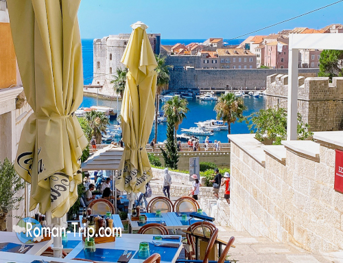 ドゥブロブニク旧港を望むテラスカフェの景色。黄色いパラソルと青いテーブルクロスが夏の地中海らしい雰囲気を演出。/ Terrace café overlooking Dubrovnik’s Old Port, where yellow parasols and blue tablecloths create a bright Mediterranean atmosphere.