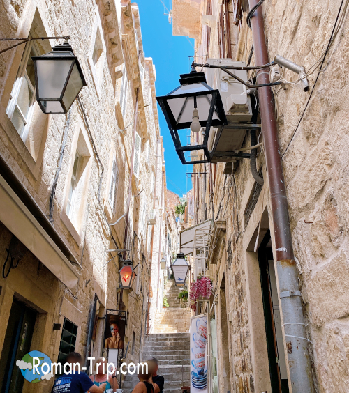 ドゥブロブニク旧市街の細い石畳の路地と階段。石造りの建物が並び、地中海の陽光が差し込む美しい街角。/ A narrow stone alley and staircase in Dubrovnik’s Old Town, lined with stone buildings and bathed in the warm Mediterranean sunlight.