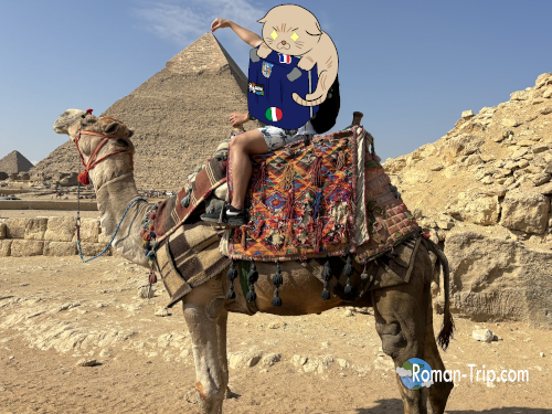 ギザのピラミッドでラクダに乗り、ピラミッドをつまむポーズで記念撮影。エジプト旅行の楽しいひととき。/ Taking a commemorative photo on a camel at the Giza Pyramids, posing as if pinching the pyramid — a joyful moment from an Egypt trip.