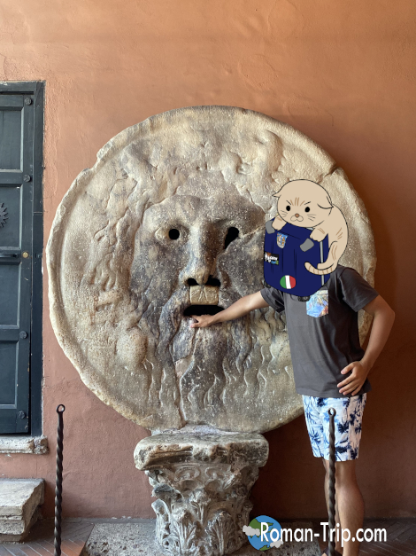 「真実の口」に手を入れて記念撮影するローマ観光の一コマ。/ Posing with a hand inside the Mouth of Truth for a memorable photo during a Rome sightseeing trip.