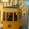 Elevador da Bica（ビッカのケーブルカー）と坂道を歩く女性を描いたイラスト。リスボンらしい風景と旅の一瞬を切り取った一枚。/ Illustration of the Elevador da Bica funicular and a woman walking up the hill — capturing a quintessential Lisbon scene and a fleeting travel moment.