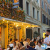 ローマひとり旅でパスタを巡る途中に出会ったおしゃれなレストラン。夏の夕暮れ、通りには多くの人々が食事を楽しんでいる。/ A stylish restaurant encountered during a solo pasta-themed walk in Rome. On a summer evening, many people are dining along the lively street.