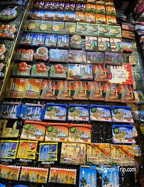お土産屋に並ぶマレーシアのご当地マグネット。青やオレンジをはじめ鮮やかな色彩が目を引くデザイン。/ Colorful Malaysian souvenir magnets on display at a shop, featuring vibrant designs in blue, orange, and other bright tones.