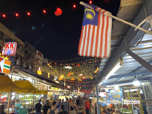 夜のジャランアロー。マレーシア国旗や明かりが輝き、活気に満ちた大通りの雰囲気。/ Jalan Alor at night, with Malaysian flags and glowing lights creating a vibrant main street atmosphere.