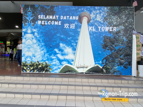 KLタワーの入り口にある「WELCOME」と書かれた看板。観光客を迎える明るい雰囲気。/ “WELCOME” sign at the entrance of KL Tower, creating a cheerful atmosphere for visitors.