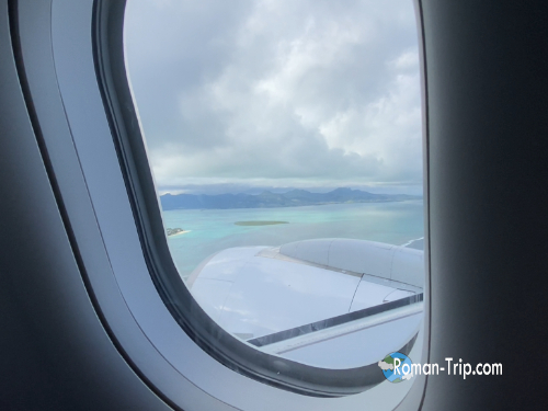 モーリシャス行きの飛行機の窓から、ついに姿を現したモーリシャスの島を望む瞬間。エメラルドグリーンの海が広がる。/ The moment Mauritius Island comes into view from the airplane window — surrounded by a dazzling emerald-green sea.