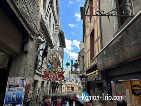 観光客でにぎわうモンサンミッシェル内部の参道。石造りの街並みに旅人たちの声が響く。/ The bustling main street inside Mont Saint-Michel, filled with tourists amid the stone-built medieval scenery.