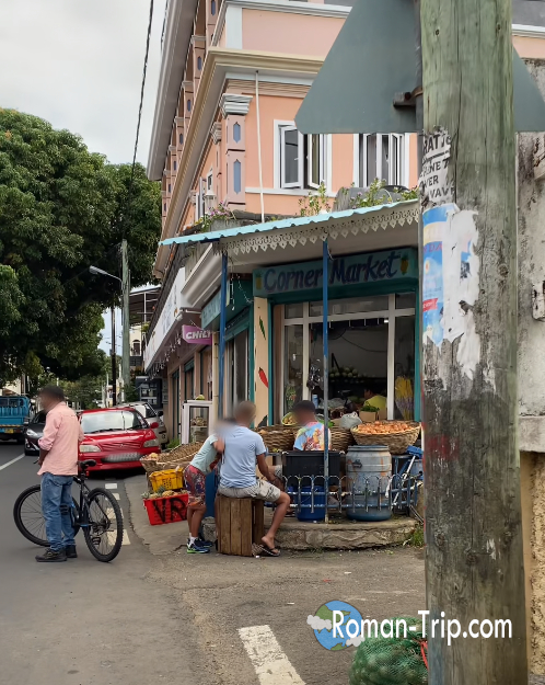 モーリシャス東部の町トゥルードースドゥースの街角マーケット。カラフルな建物の前で人々が語らうローカルな風景。/ Corner market in Trou d’Eau Douce, eastern Mauritius, where locals gather and chat in front of colorful colonial-style buildings.
