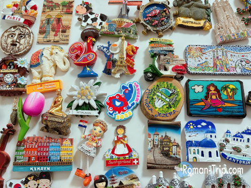 世界中で集めたご当地マグネット。スイスやサントリーニ島など、色鮮やかで個性的なデザインが並ぶ。/ A collection of souvenir magnets from around the world, featuring colorful and unique designs from places like Switzerland and Santorini.