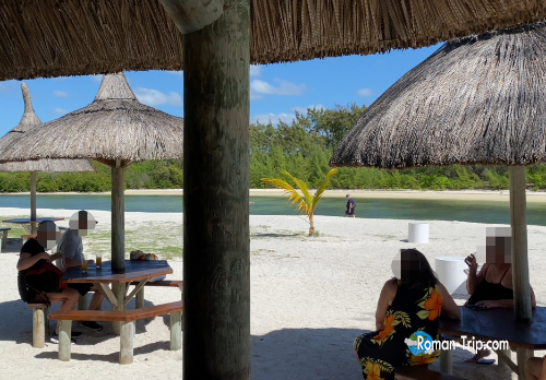 モーリシャスのイル・オ・セルフ島のビーチ。ヤシ葺き屋根のパラソルの下で観光客がくつろぐ南国の楽園。/ Beach scene on Île aux Cerfs, Mauritius — tourists relaxing under thatched parasol huts on a serene tropical shore.