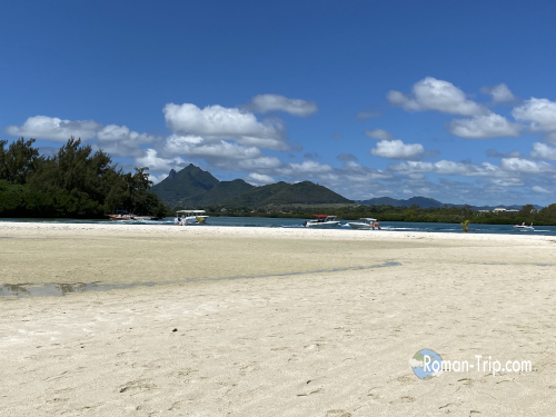 モーリシャスのイル・オ・セルフ島、ラグーンの対岸に見える景色。白い砂浜の向こうに山々が連なる穏やかな風景。/ View of the opposite shore of the lagoon at Île aux Cerfs, Mauritius — calm scenery with white sand and distant green mountains.