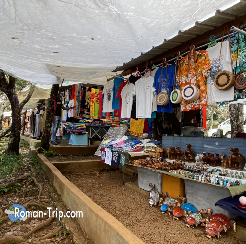 モーリシャスのゴルジュ展望台にあるローカルなお土産屋。Tシャツや木彫り雑貨などが並ぶ、自然に囲まれた素朴な売店。/ A local souvenir shop at the Gorges viewpoint in Mauritius, displaying T-shirts and handcrafted wooden items in a rustic, nature-filled setting.