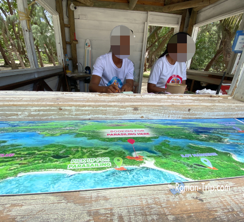 イル・オ・セルフ島にあるマリンアクティビティの受付カウンター。地図を見ながらスタッフが手続きを行う南国らしいローカル感あふれる一角。/ Reception counter for marine activities at Île aux Cerfs, Mauritius — staff assisting visitors with bookings over a colorful activity map.