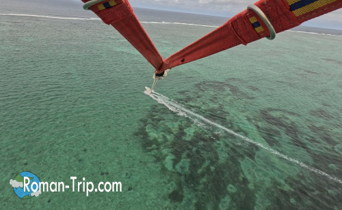 イル・オ・セルフでのパラセイリング中、空から見下ろしたエメラルドグリーンのラグーン。海上を走るボートの航跡が美しいコントラストを描く。/ Aerial view during parasailing at Île aux Cerfs, Mauritius — an emerald-green lagoon below and the boat’s wake tracing a white line across the sea.