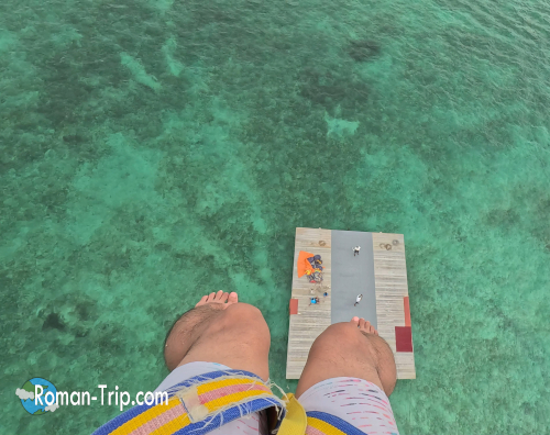 イル・オ・セルフでのパラセイリング中、ひとりで空を飛びながら着地台を見下ろす瞬間。足元に広がるエメラルド色の海と、これから自分で着地するドキドキ感。/ Solo parasailing at Île aux Cerfs, Mauritius — looking down at the landing platform with emerald waters below, capturing the thrill of preparing to land on your own.