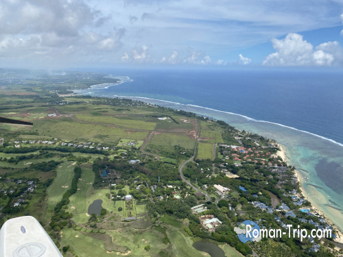 モーリシャスの海の滝フライト序盤にセスナから見下ろした海岸線と緑豊かな大地。上空から広がる島の景色が一気に視界に入る瞬間。 / An early-stage view from the seaplane flight over Mauritius, showing the coastline and lush green landscape spreading out below just after takeoff.