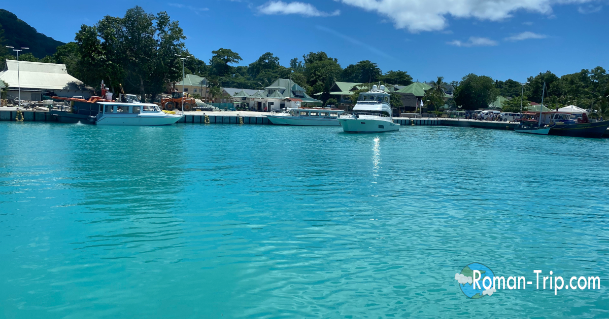 船で訪れたセーシェルのラディーグ島の港。エメラルドブルーに輝く海と停泊するボートが、南国の楽園らしい風景をつくり出している。 / The emerald-blue waters of La Digue Island in Seychelles seen upon arriving by boat, with moored boats and a tropical island harbor scene.