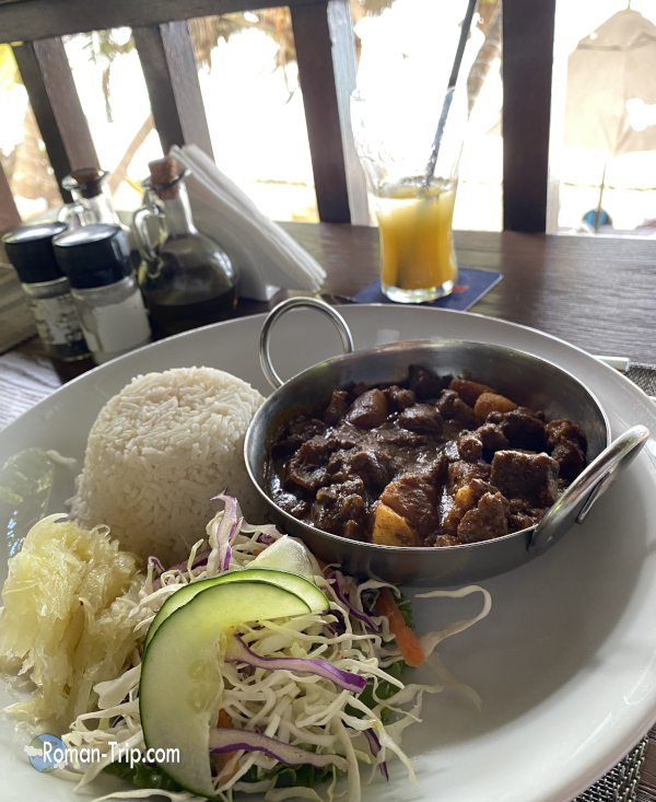 セーシェル・マヘ島で食べたヤギ肉カレーとオレンジジュース。旅先の食堂で味わった現地らしい食事風景。/ Goat curry and orange juice enjoyed on Mahé Island, Seychelles, a local-style meal scene at a restaurant during the trip