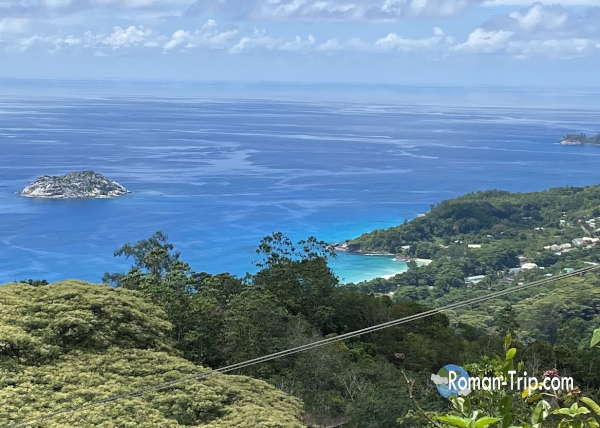 セーシェル・マヘ島の高台から見下ろした青く輝くビーチの遠景。思わず見惚れてしまうほど美しいインド洋のグラデーション。 / A distant panoramic view of a stunning blue beach on Mahé Island in Seychelles, with mesmerizing gradients of the Indian Ocean.