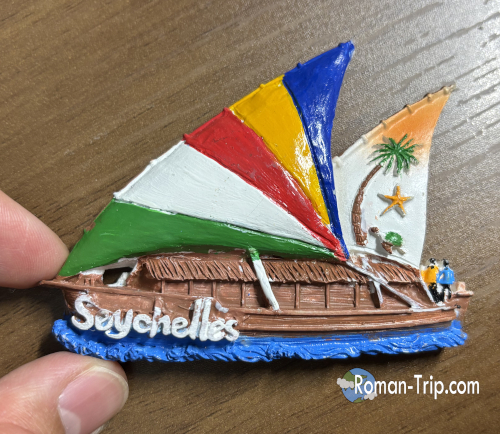 セーシェル国旗のカラーをモチーフにした帆船デザインのご当地マグネット。南国らしい海の国セーシェルを象徴するお土産。 / A souvenir magnet shaped like a sailboat featuring the colors of the Seychelles flag, representing the island nation's maritime culture.