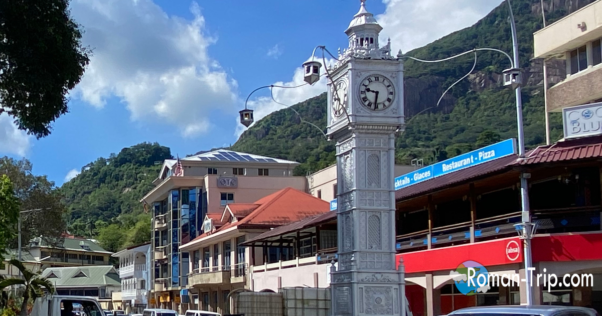 セーシェルの首都ヴィクトリアを歩いたときの街並み。街のシンボルである時計塔と、山に囲まれた南国の小さな首都の風景。 / Street scene from a walk in Victoria, the capital of Seychelles, featuring the iconic clock tower and the tropical town surrounded by green mountains.
